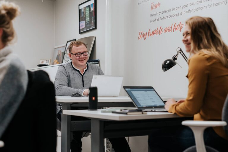 Hymyilevä mies ja nainen jaetussa työhuoneessa omilla työpisteillään coworking-tilassa