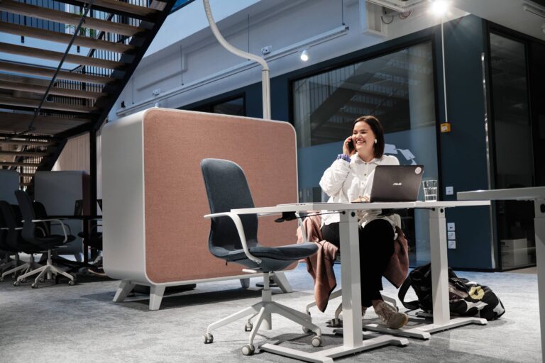 Nainen puhumassa iloisesti puhelimeen yhteiskäyttöisessä toimistossa coworking-tilassa, toimiston vuokraaminen